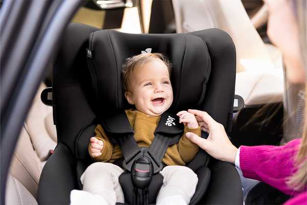 A happy baby being swivelled in a Joie i-Spin 360™ car seat by her parent.